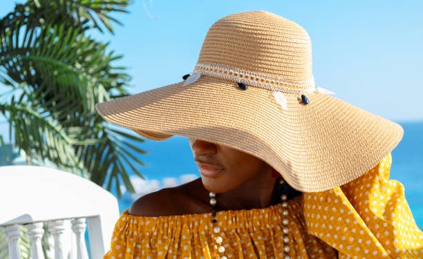 Portrait of beautiful African American model girl in stylish sun hat. Fashion black woman on natural background coast of sea. High quality photo