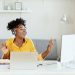 Happy African American Businesswoman Having Fun While Working at Office Desk and Listening Music Over Headphones. Relaxed Young Woman in Headphones Enjoying Music Podcast Using Laptop App, Smiling Female Millennial Student or Office Worker Wearing Headset Listening to New Favorite Audio Tracks at Home or Work
