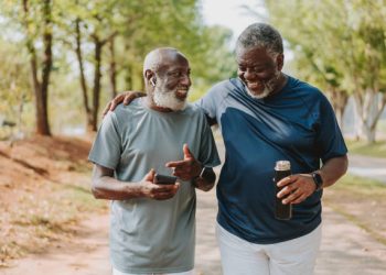 Two black senior friends walking together in public park