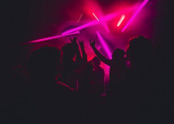 People dancing in a nightclub with smoke machines and strobe lighting around them.
