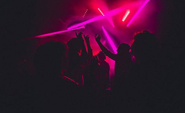 People dancing in a nightclub with smoke machines and strobe lighting around them.