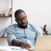 Bored lazy African American executive manager looking at laptop screen having no motivation. Black tired, sleepy, overworked employee feeling lack of energy sitting at office table front of computer